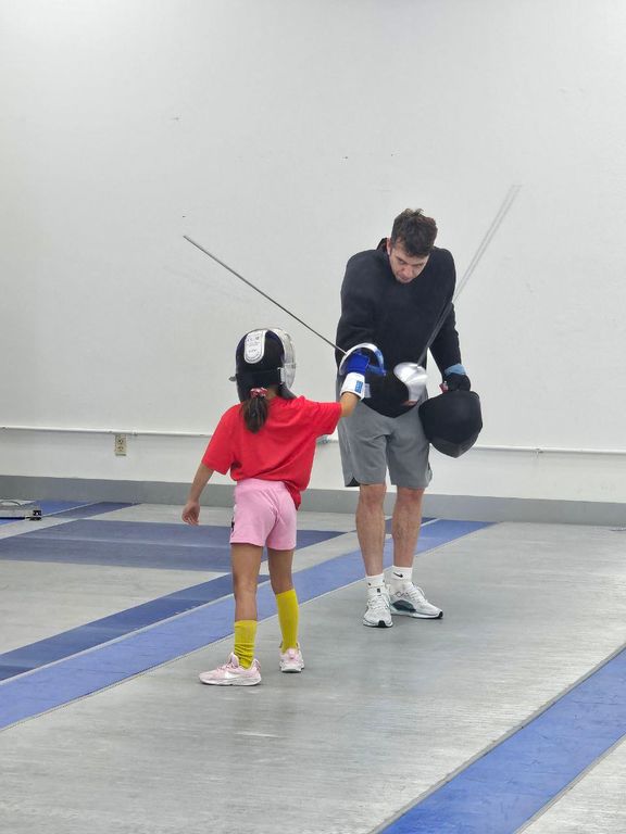 A coach helps a young beginner with her mask on the strip